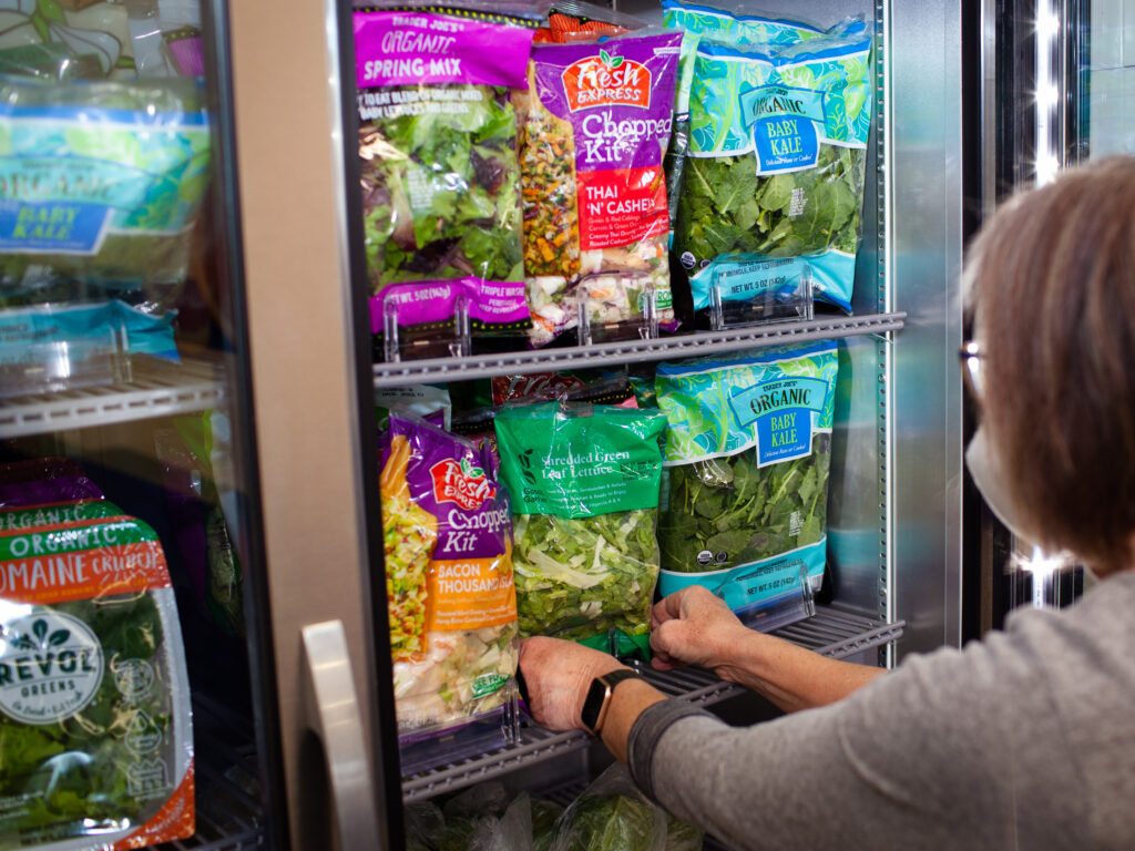 a woman in a gray shirt putting salad into a cooler filled with other salad items